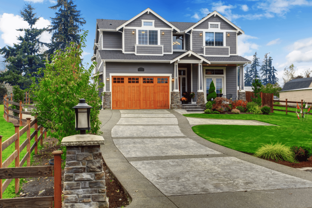 A large home with a stone driveway, beautiful trees, green grass, shrubs and flowers